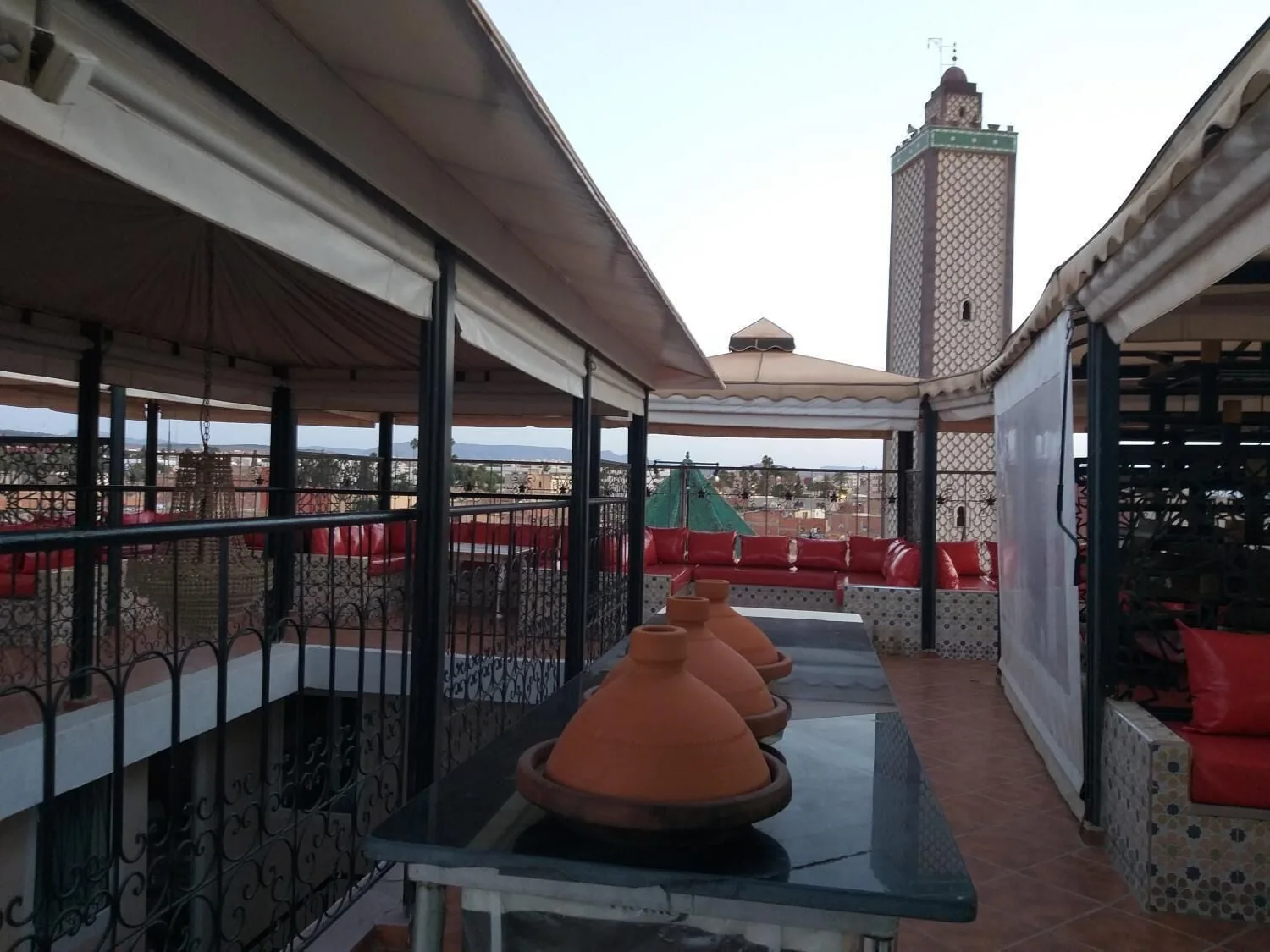Terrasse du riad, banquettes rouges et minaret au-dessus des toits d’Oujda